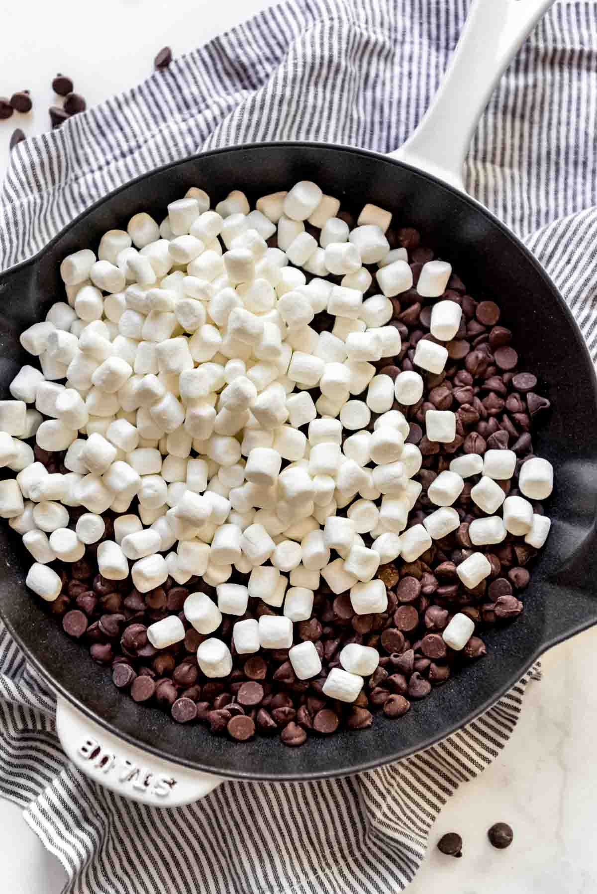 Mini marshmallows are placed on top of chocolate chips in a cast iron skillet. 