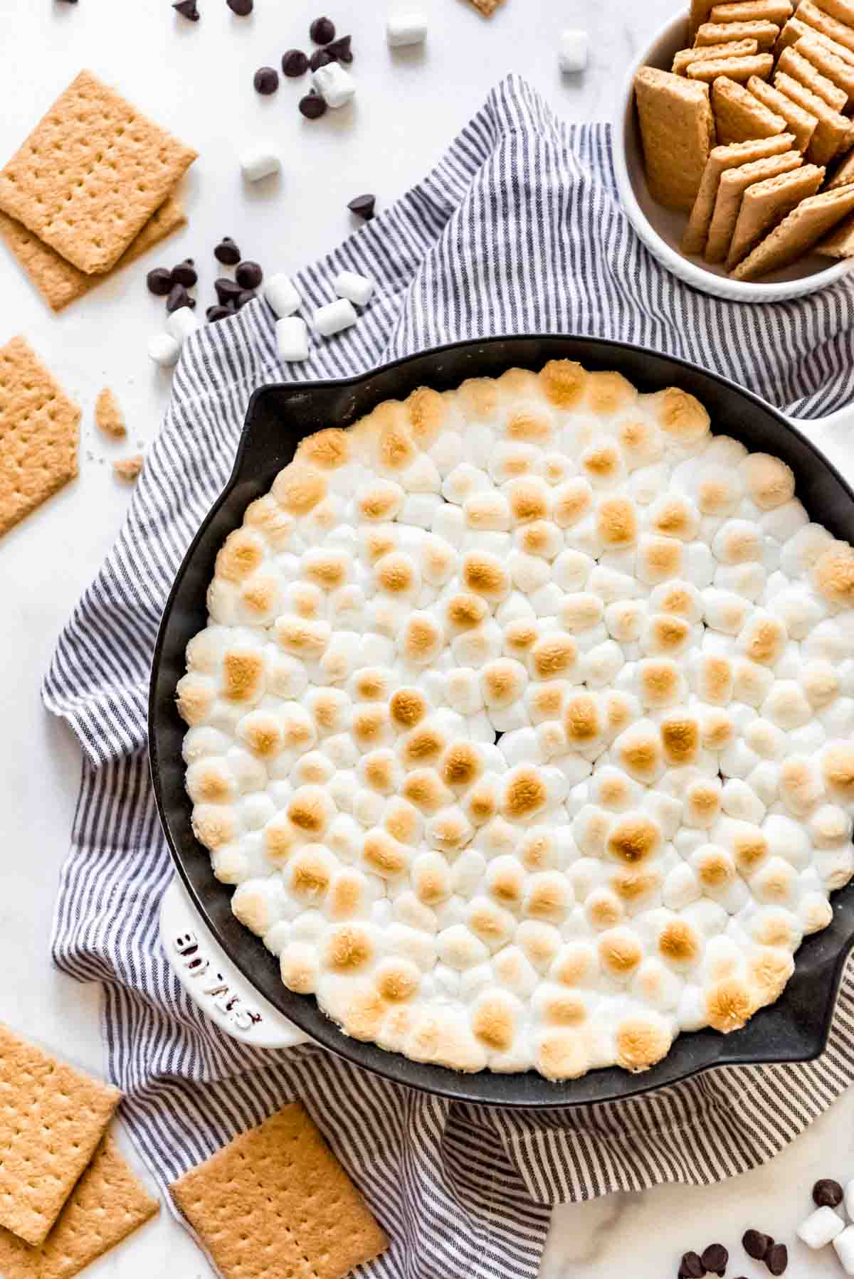 Toasted marshmallows top a s'mores dip dessert that's been baked in a cast iron skillet. 