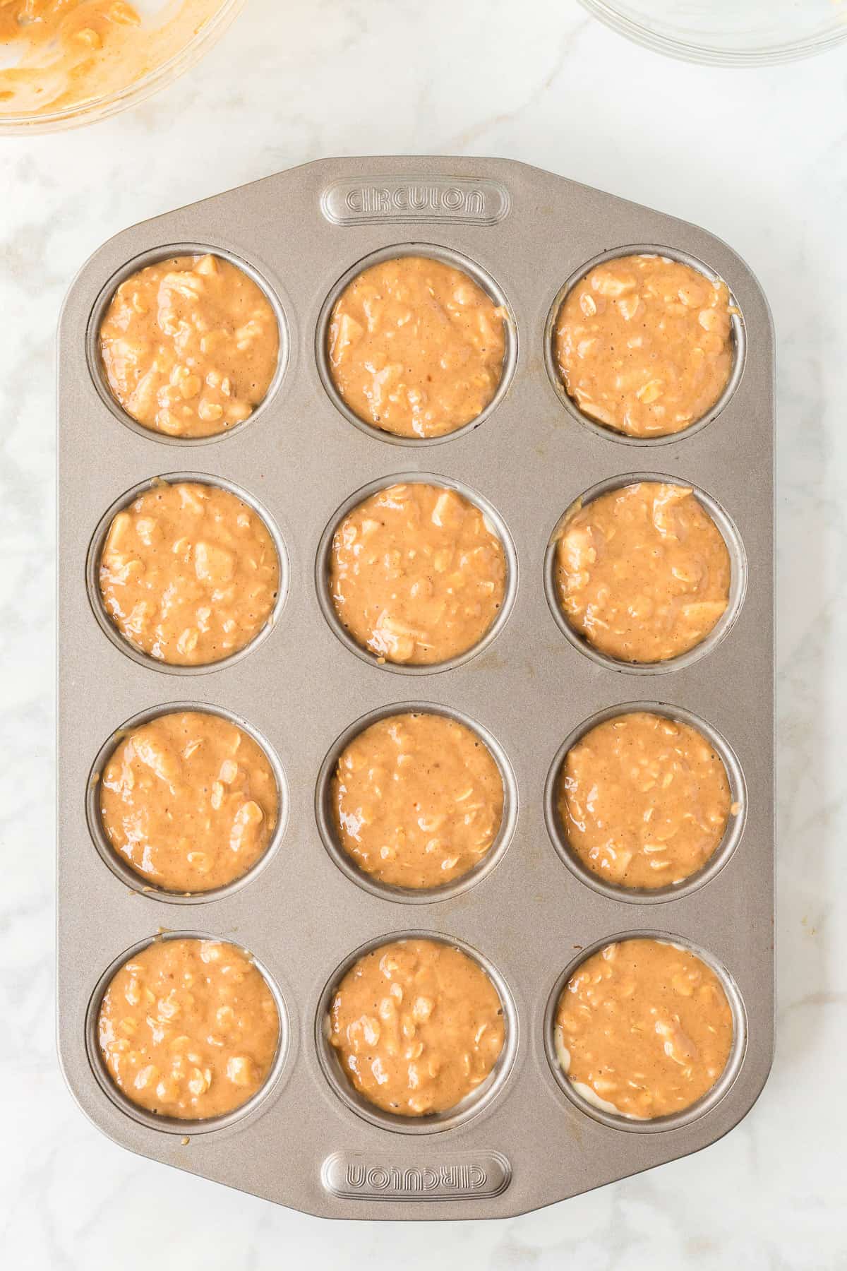 apple oatmeal muffin batter in a greased muffin pan.