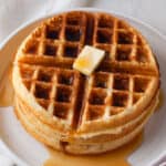 A stack of homemade Belgian waffles with a pat of butter and maple syrup on them.
