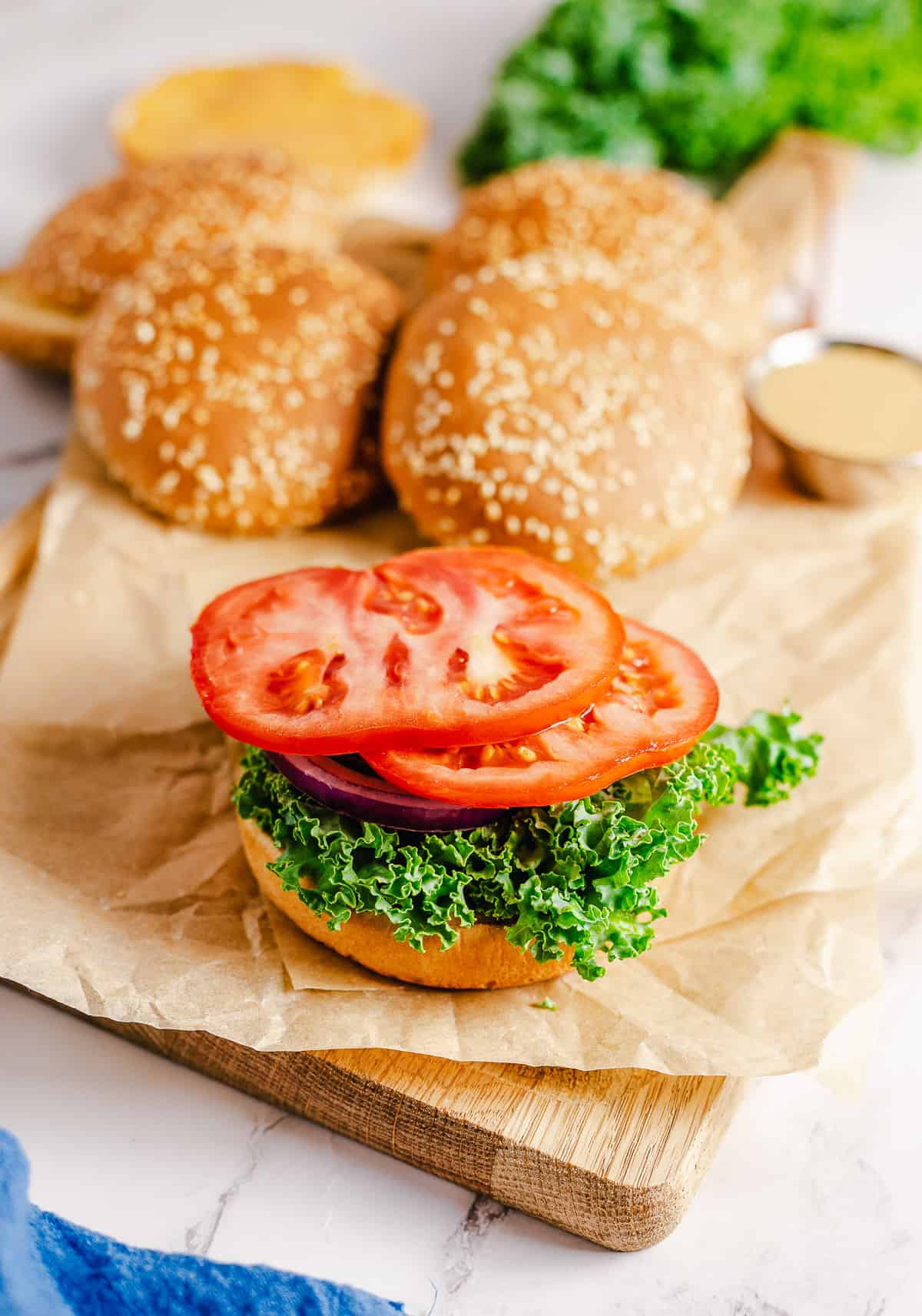 Lettuce, onion, and sliced tomato layered on a hamburger bun on a cutting board.