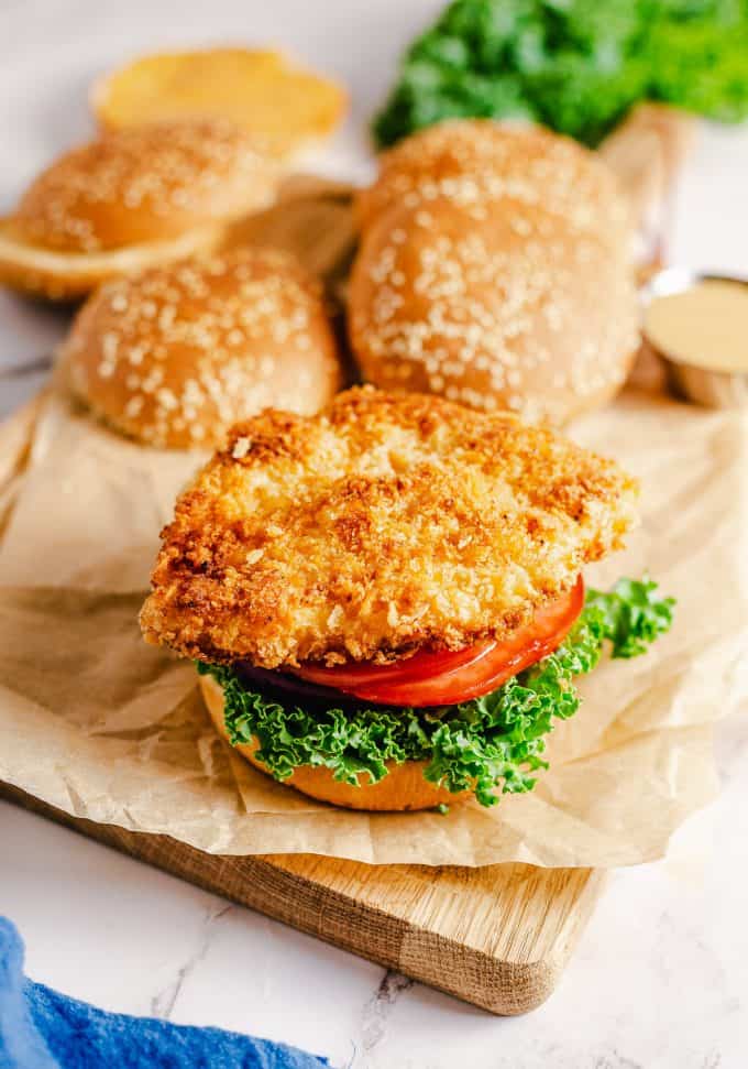 Adding crispy chicken on top of lettuce, tomato, and onion for a chicken sandwich.