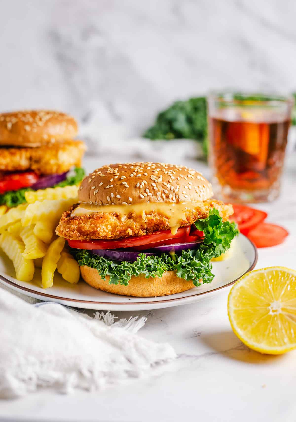 A crispy chicken sandwich on a plate with fries next to a lemon  half.