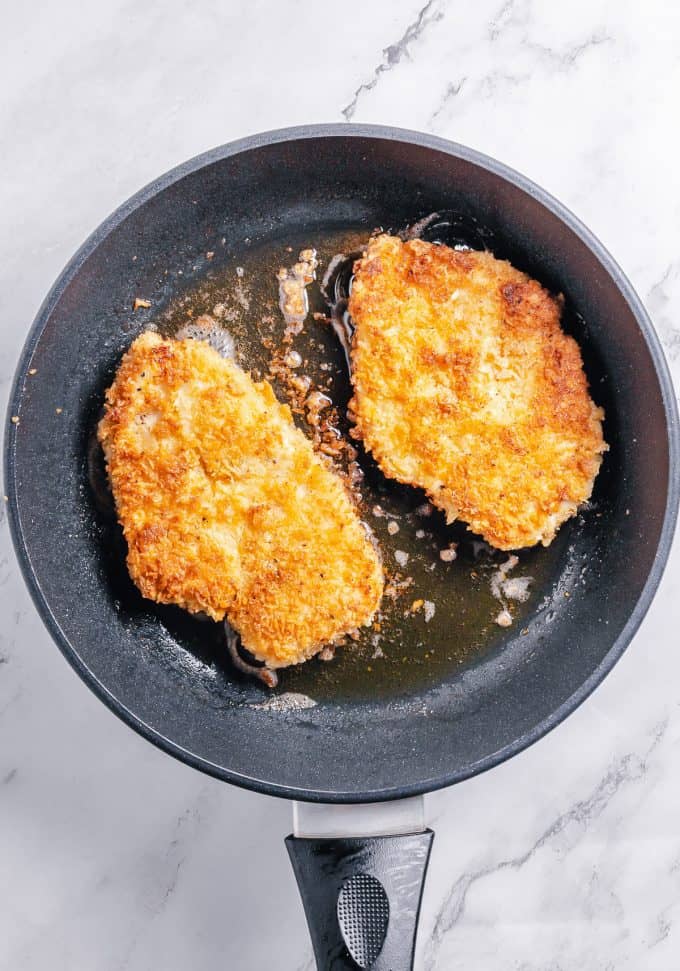Crispy chicken breasts that have just been flipped in a pan of oil and are brown on one side.