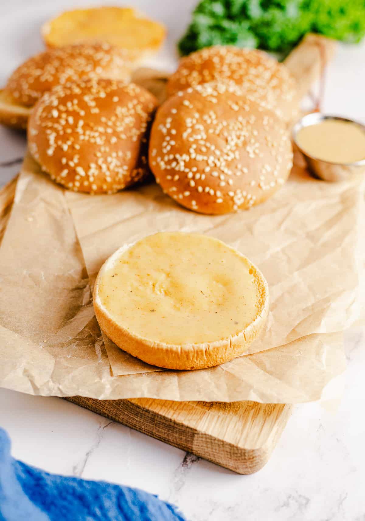 Sauce on a bottom hamburger bun on a cutting board.