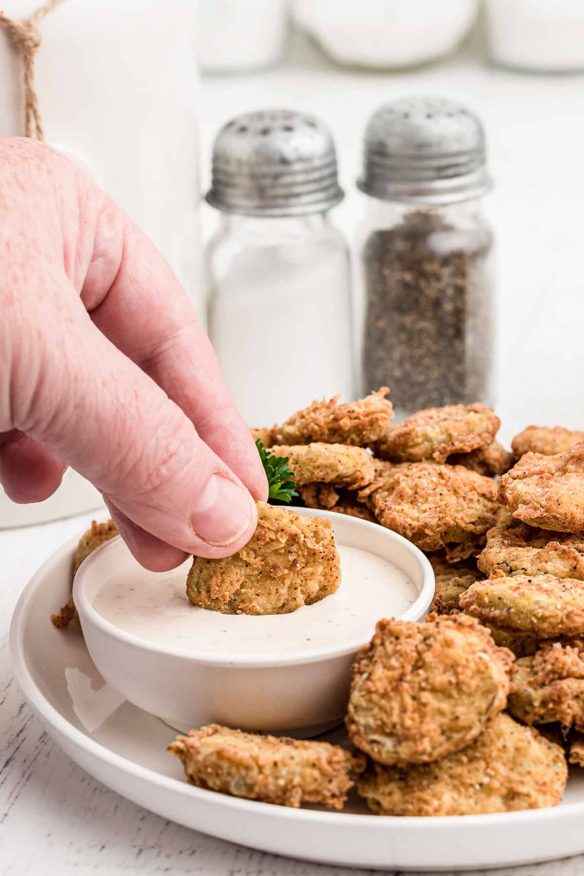 A hand dipping a fried pickle into a small bowl of sauce. 