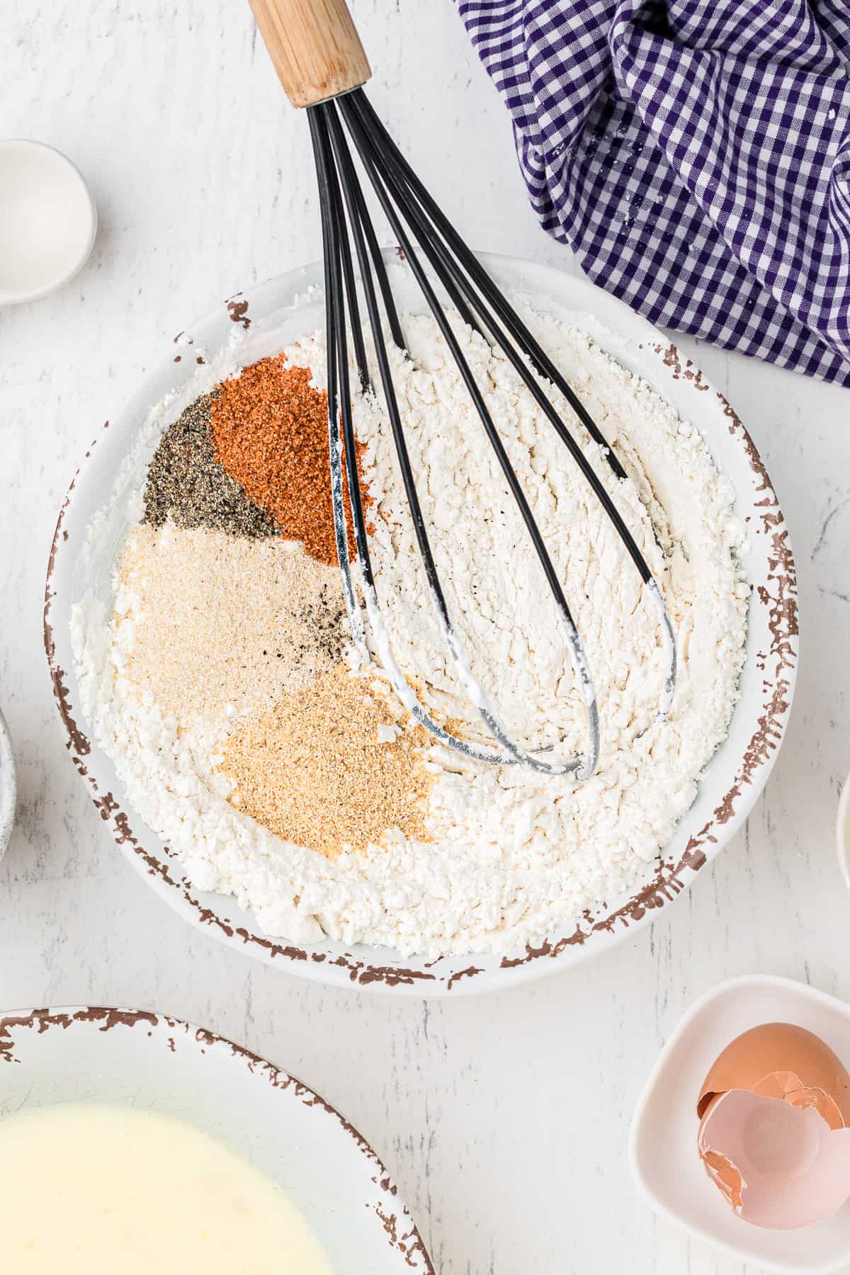 Spices like garlic powder, onion powder, pepper, and creole seasoning with flour in a bowl.