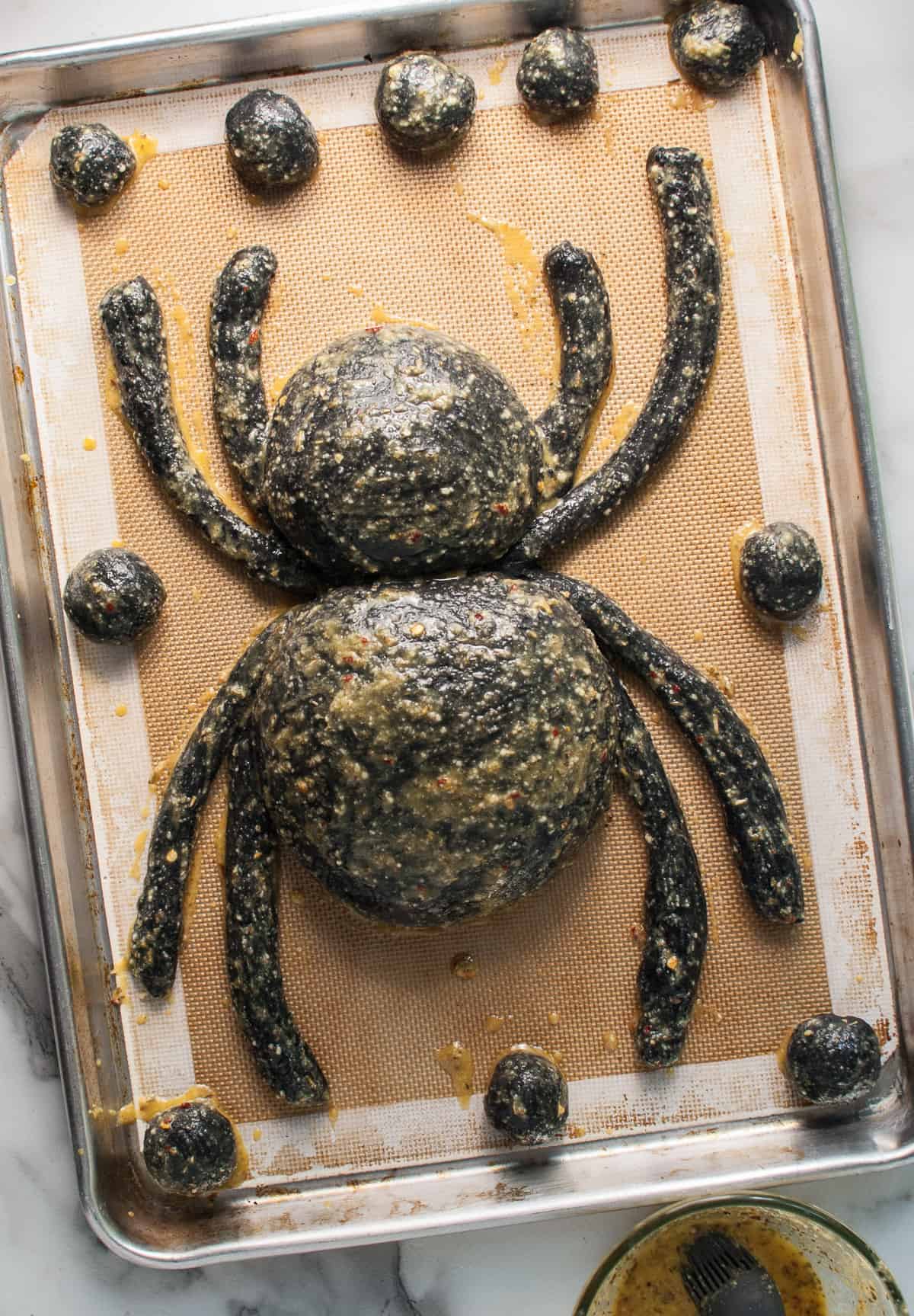 A Halloween appetizer bread bowl shaped like a spider brushed with garlic herb egg wash.