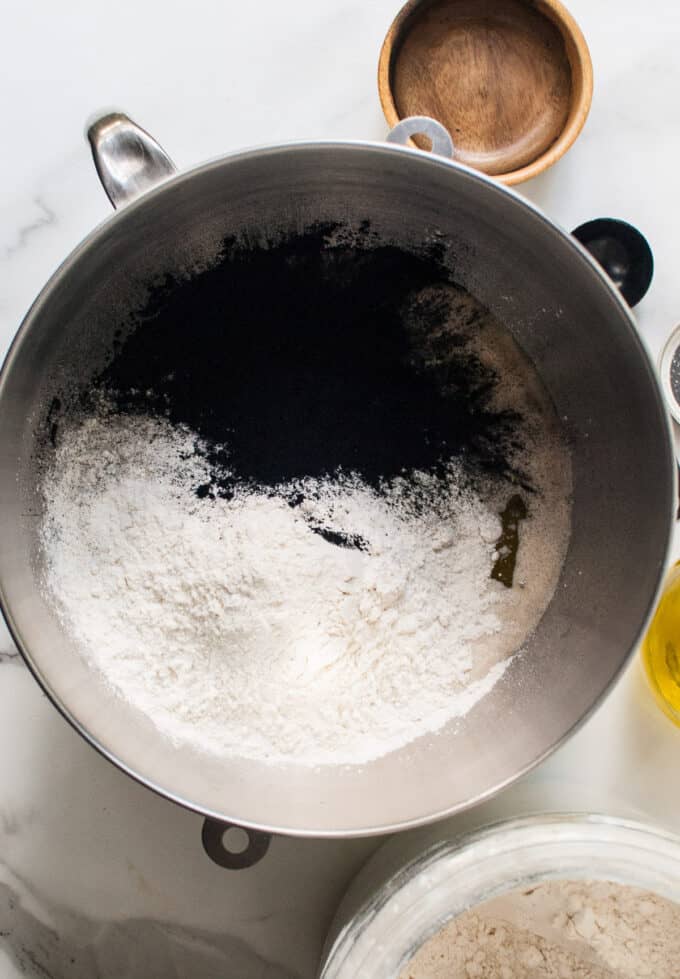 Adding flour and activated charcoal powder to active yeast in a bowl.