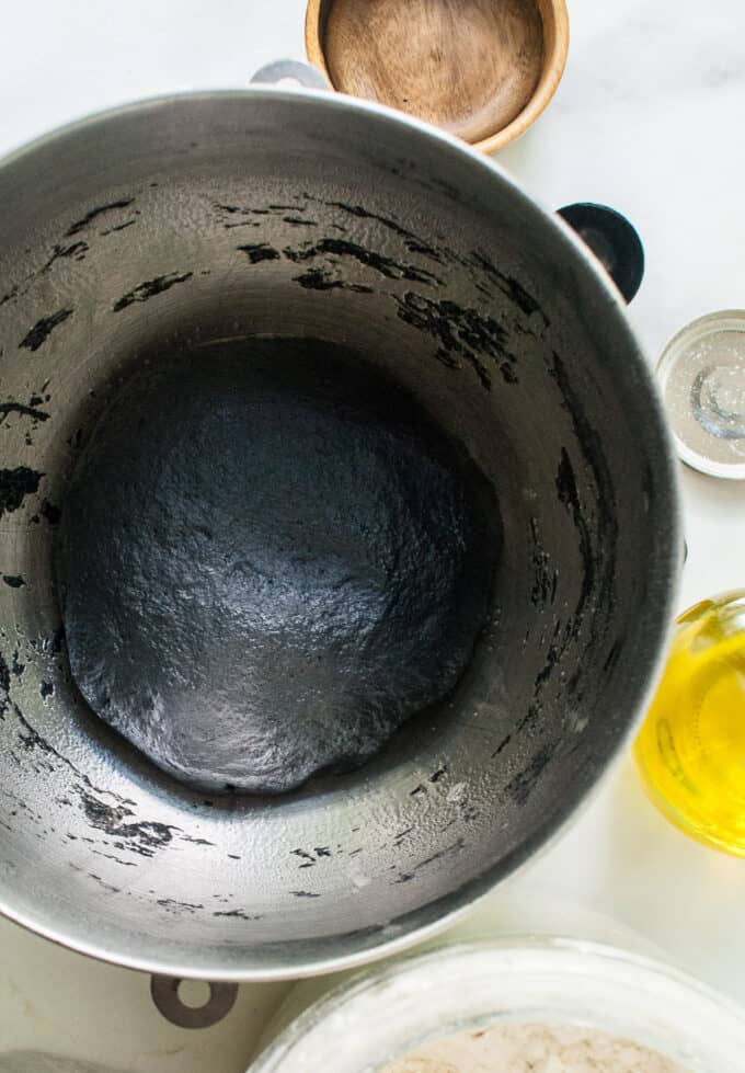 A ball of bread dough made with activated charcoal powder rising in a greased bowl.