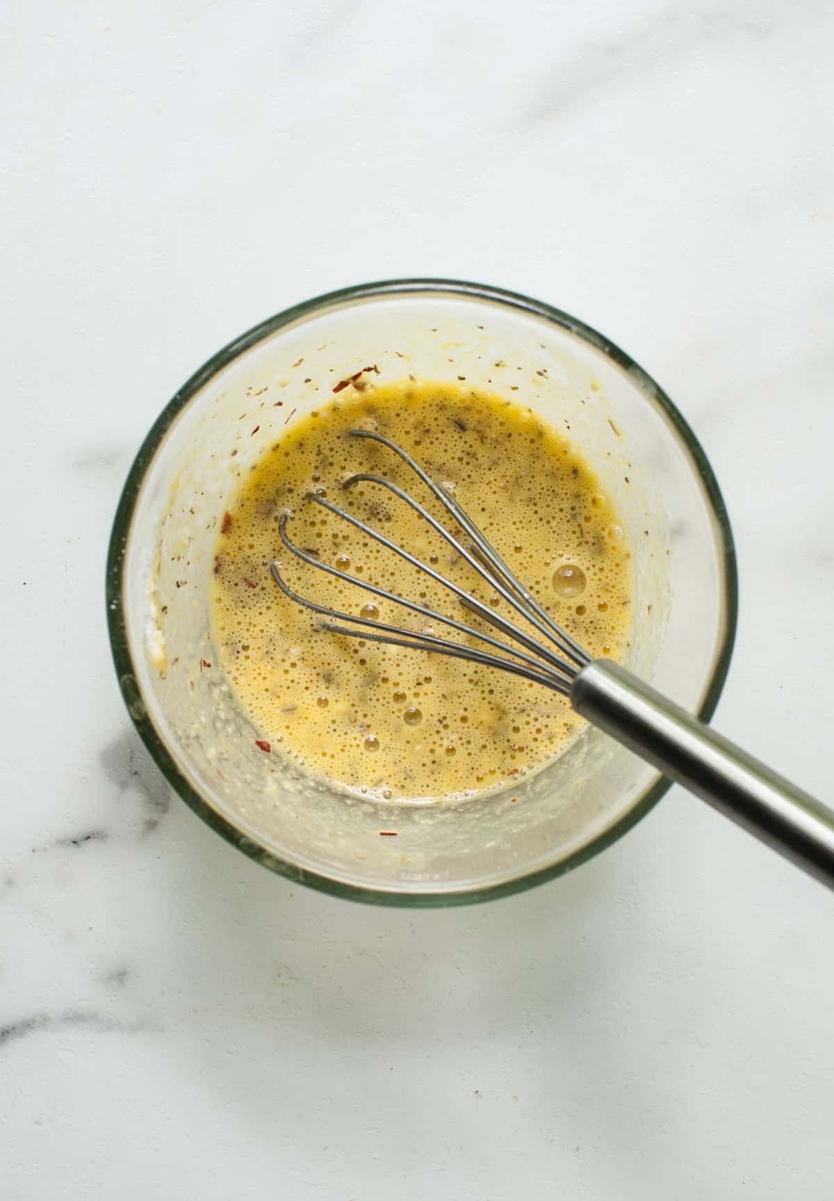 A garlic and herb egg wash in a bowl with a whisk.