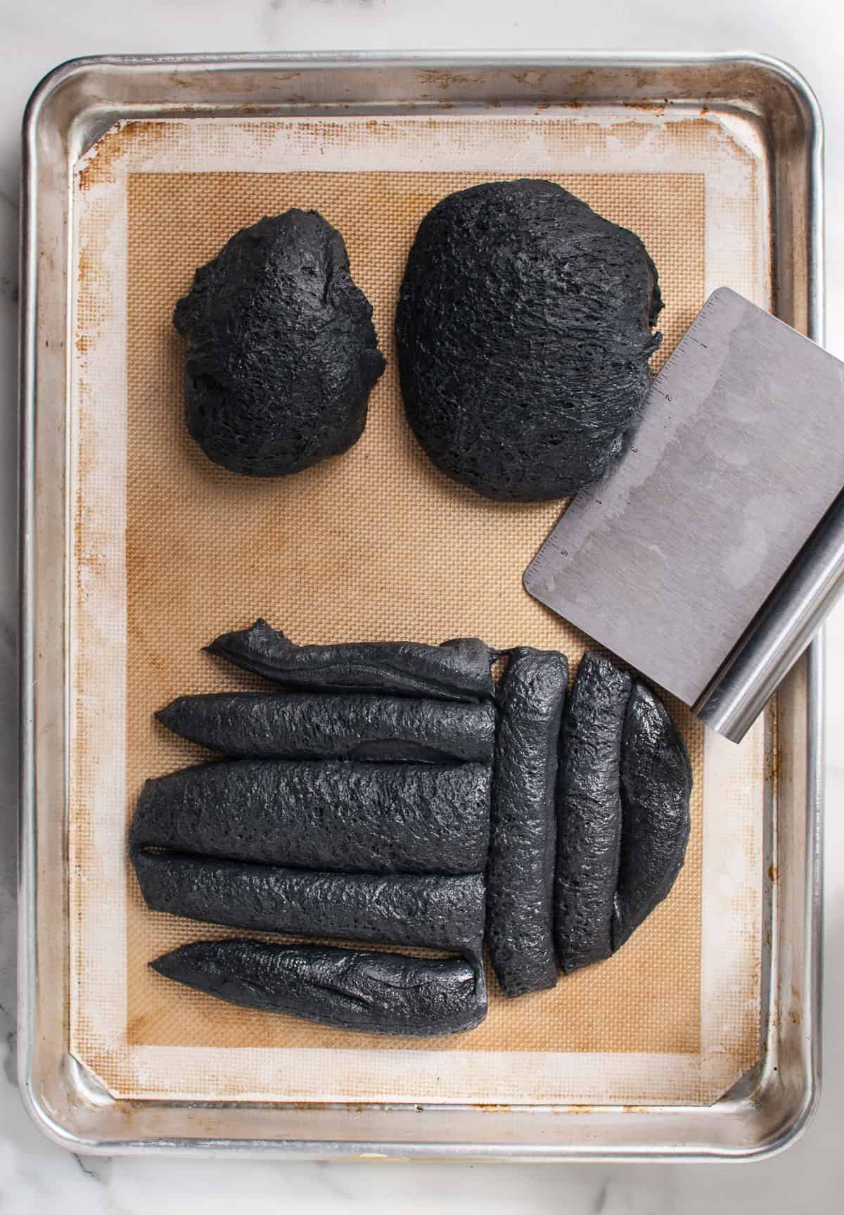 Black bread dough divided into pieces for shaping into a spider.