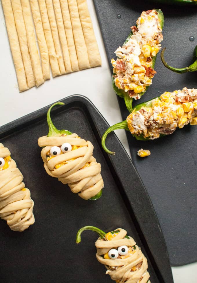 Jalapeno poppers wrapped in thin strips of crescent roll dough with candy eyes place to look like mummies for Halloween.