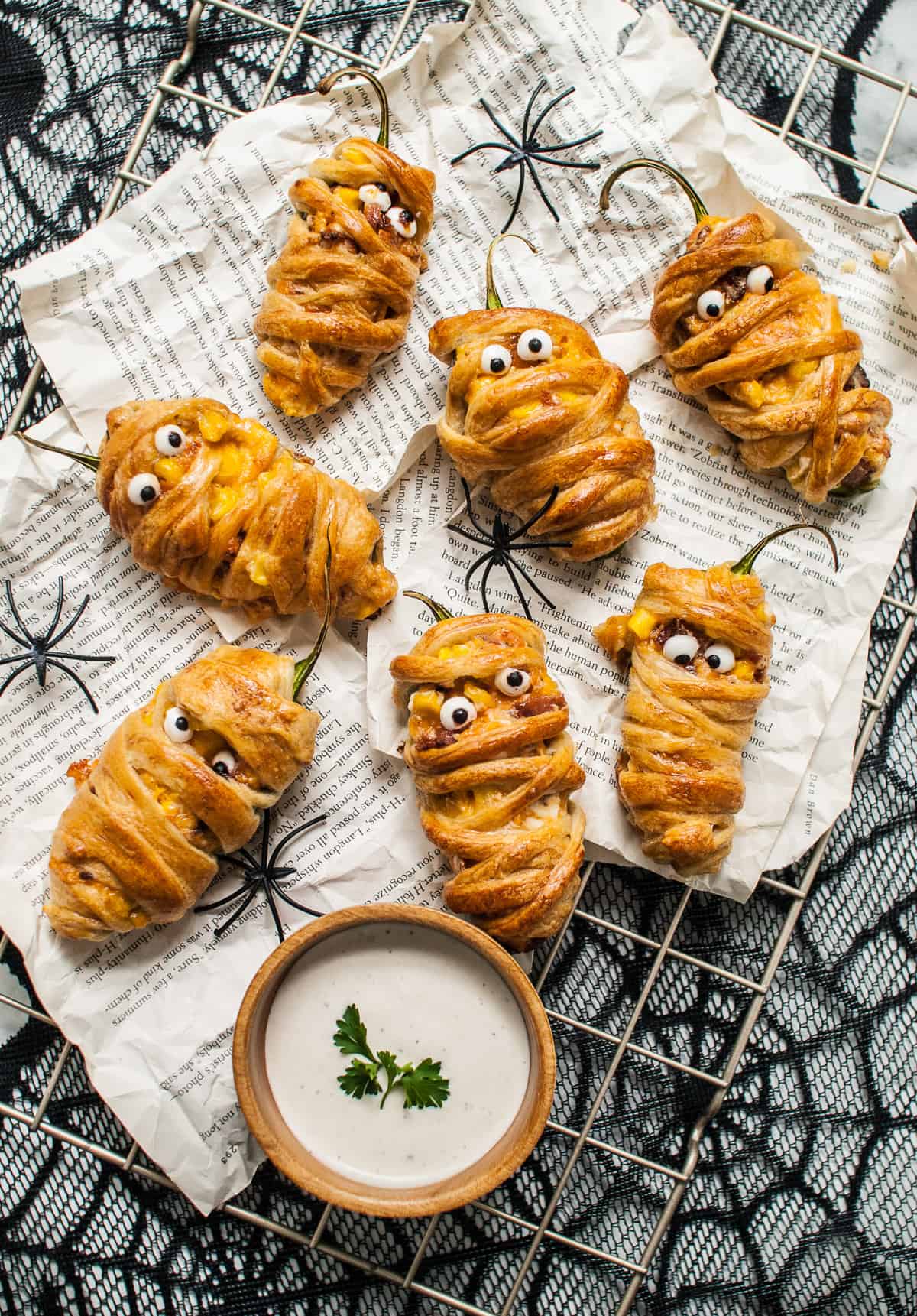 Mummy jalapeno poppers made with candy eyes next to a bowl of ranch sauce for dipping.