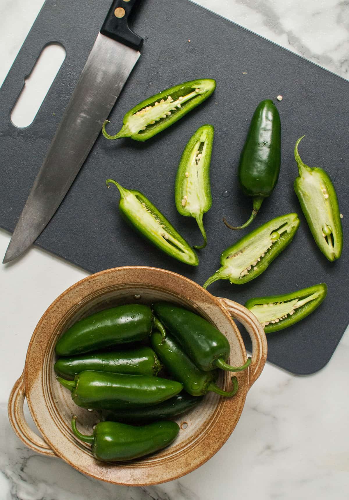 Fresh jalapenos sliced in half on a grey cutting board.