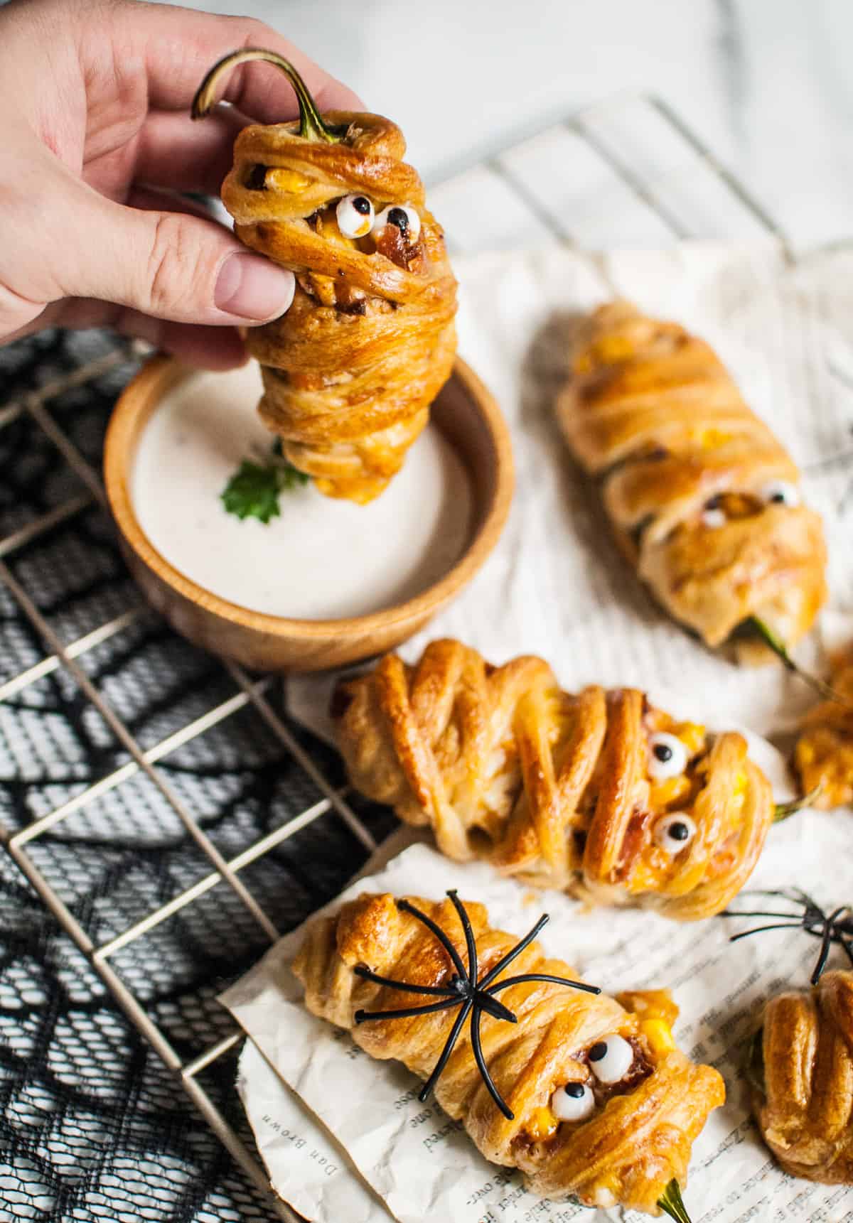 A hand dipping a Halloween mummy jalapeno popper into ranch sauce.