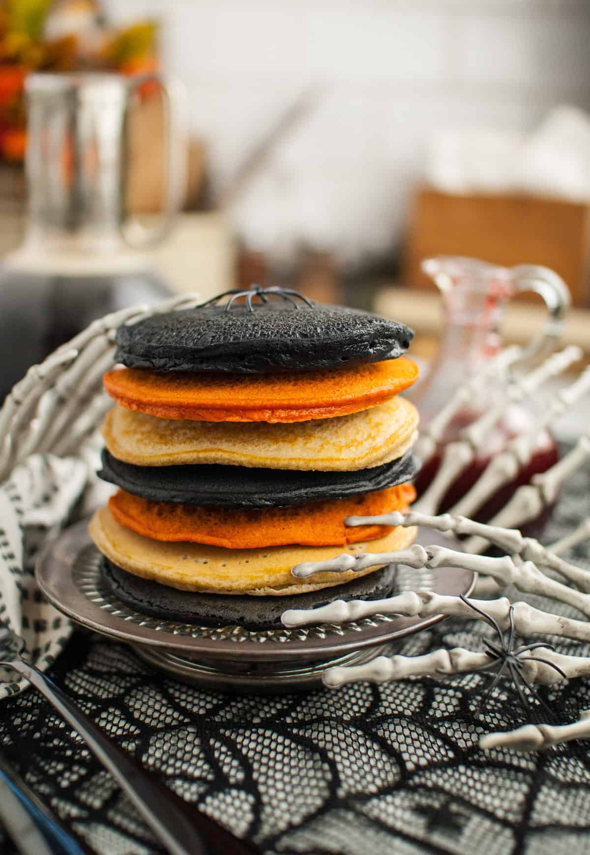 A stack of black, orange, and white pancakes with plastic skeleton hands next to it.