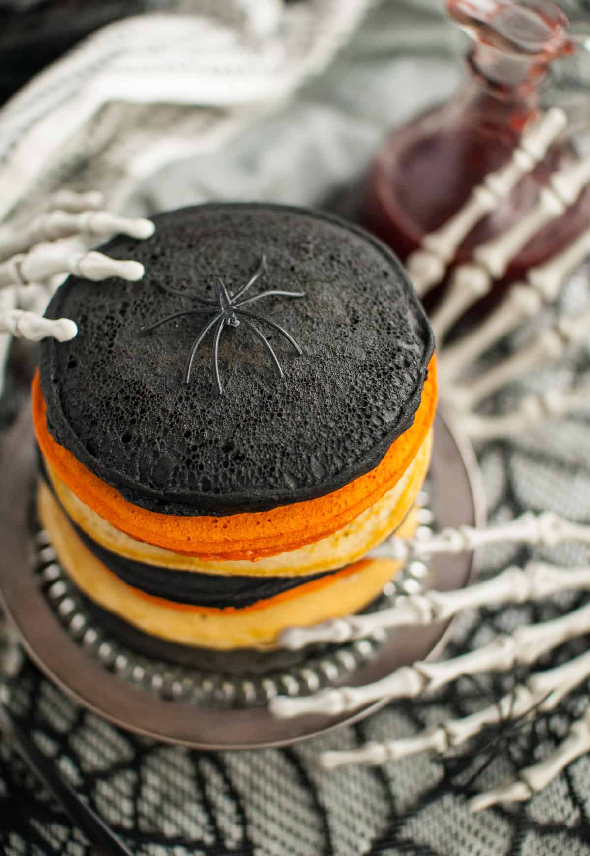 A plastic spider sitting on top of a stack of pancakes dyed with food dye and activated charcoal powder for Halloween.