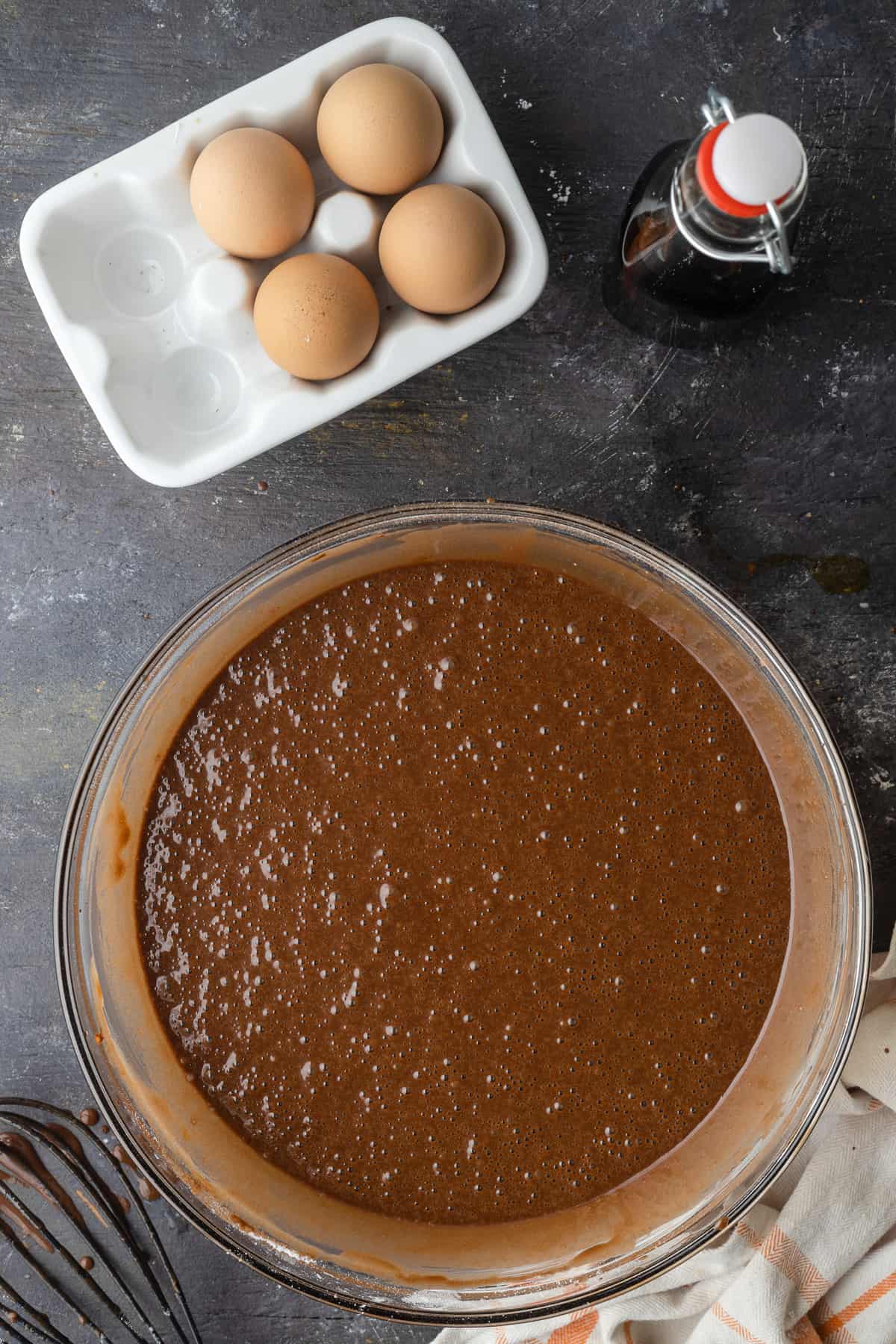 Chocolate cupcake batter in a bowl next to eggs and vanilla extract.