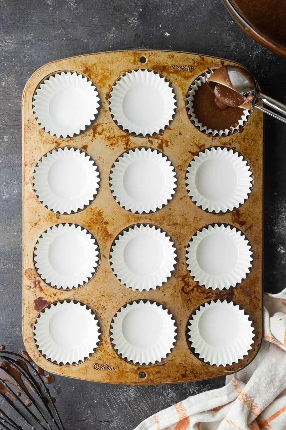 Using a cookie scoop to fill white cupcake liners.