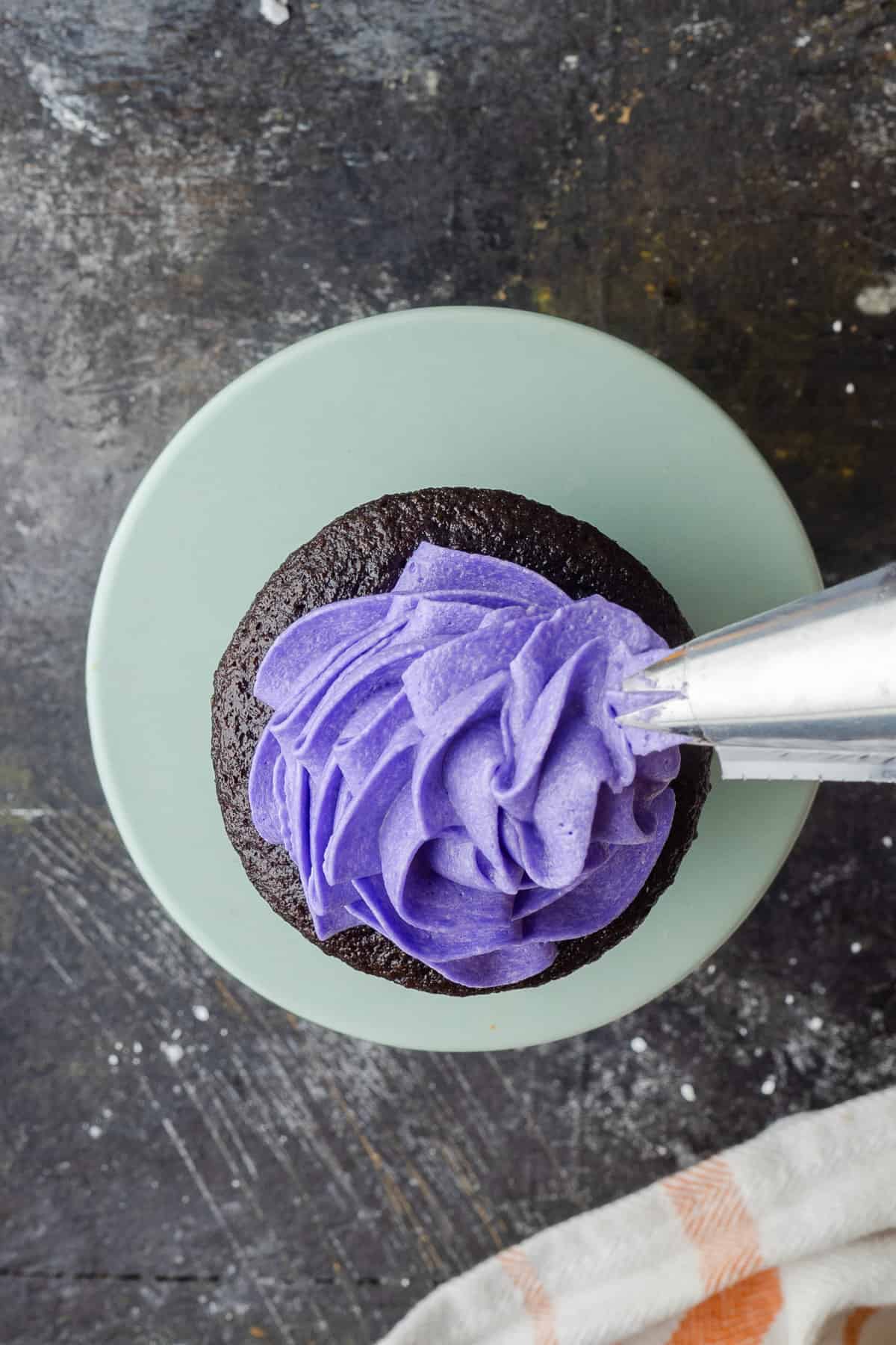 Using the piping tip to pull the swirl of purple frosting off the side of the cupcake for a lopsided appearance.