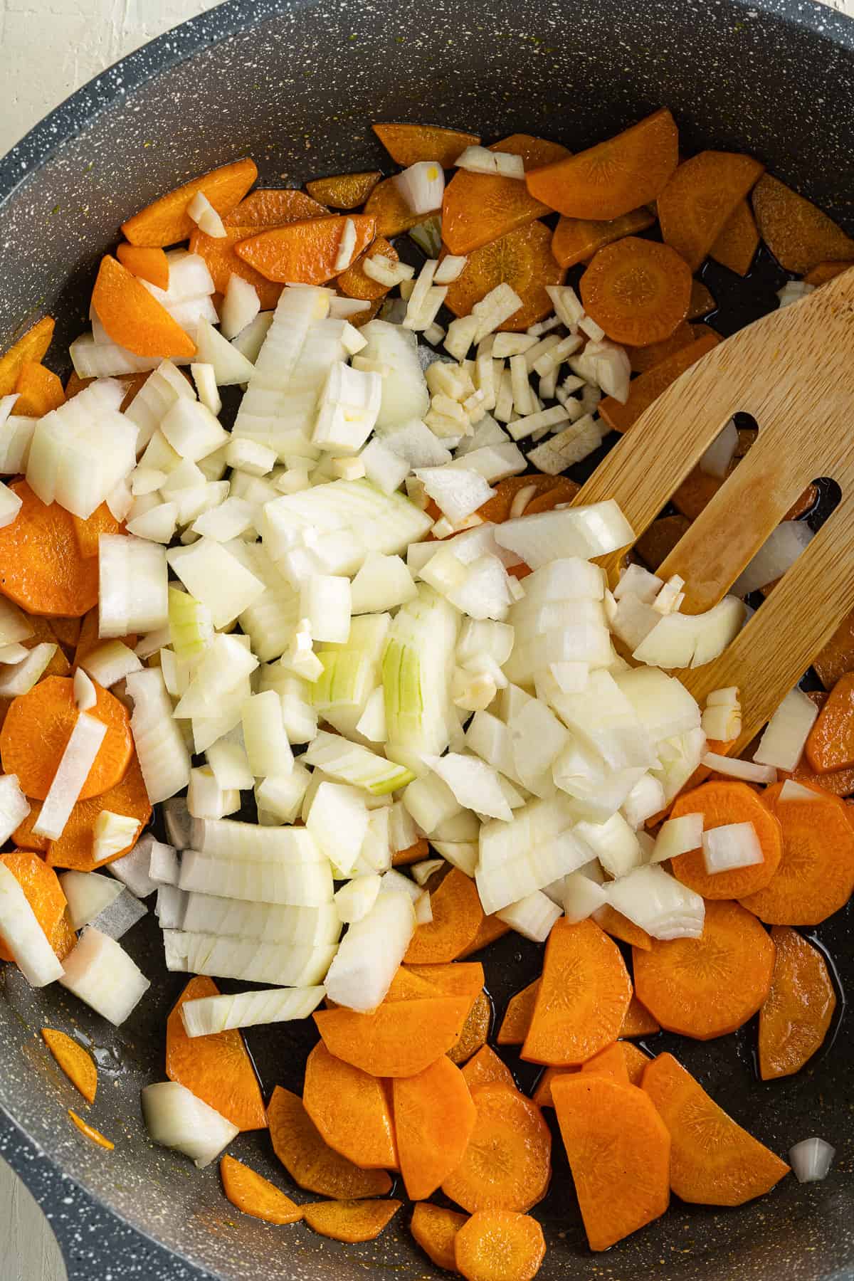 Top view of a black pot with chopped carrots, onions, and garlic in it.