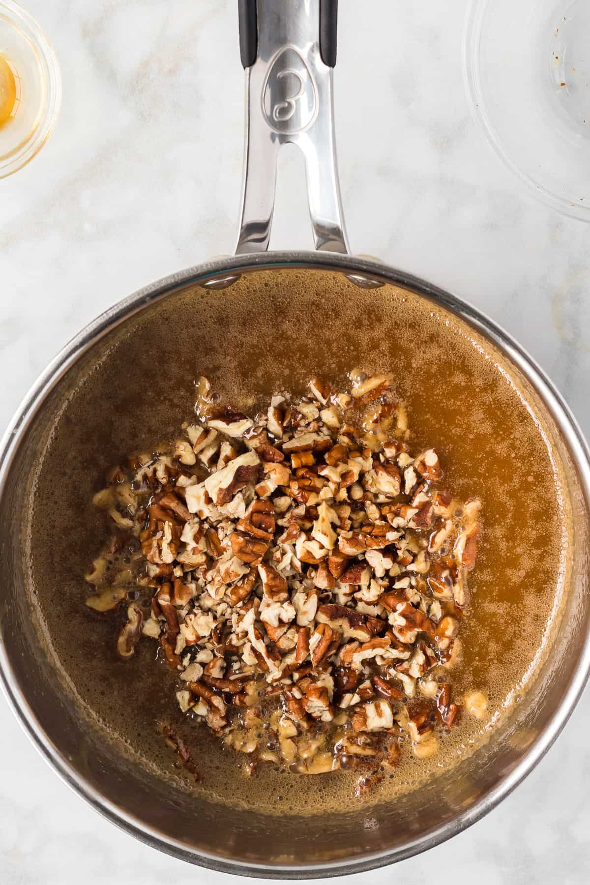 Adding pecans to a caramel syrup mixture in a medium saucepan.