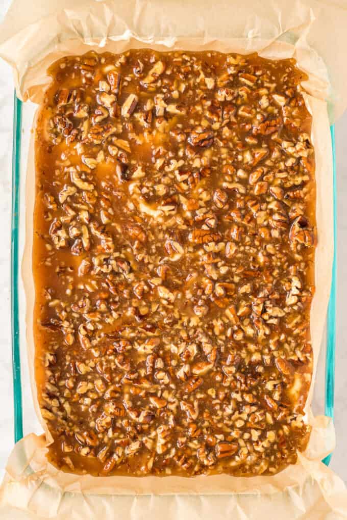 Pouring pecan pie filling over cheesecake bars before baking.