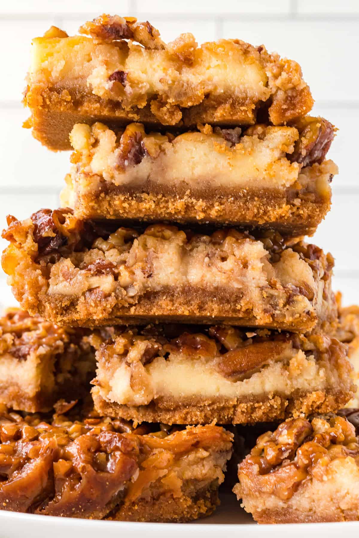 A stack of creamy cheesecake bars with pecan pie filling on top and a graham cracker crust.