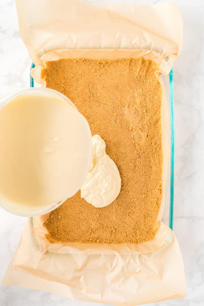 Pouring cheesecake filling over a graham cracker crust in a 9x13-inch pan.