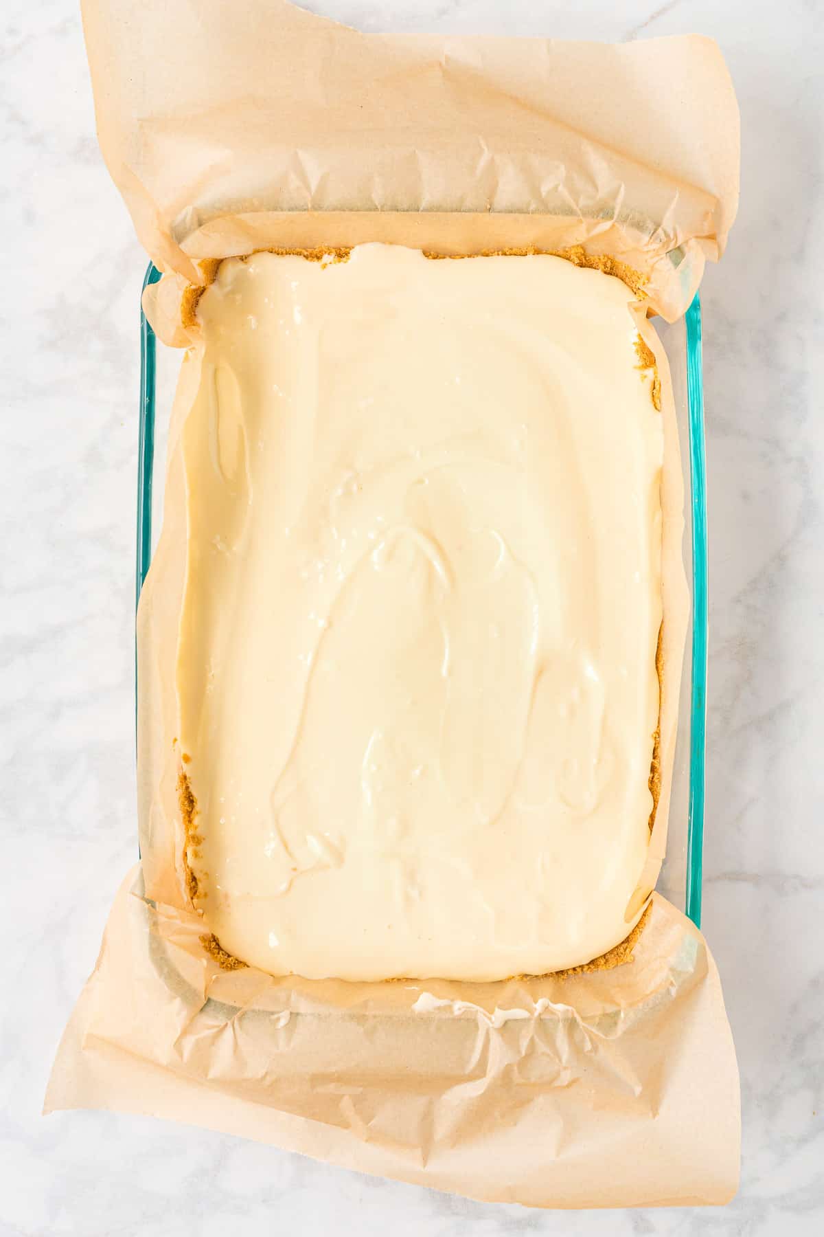 Smoothing out the top of cheesecake bars in a glass baking dish.