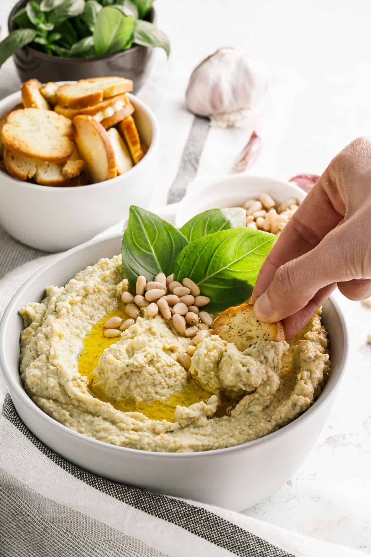 A hand dipping a bagel chip into a bowl of homemade hummus.