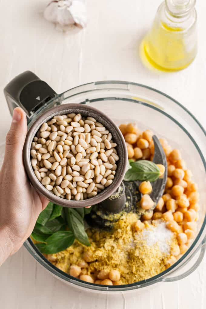 Adding pine nuts to hummus ingredients in a food processor.