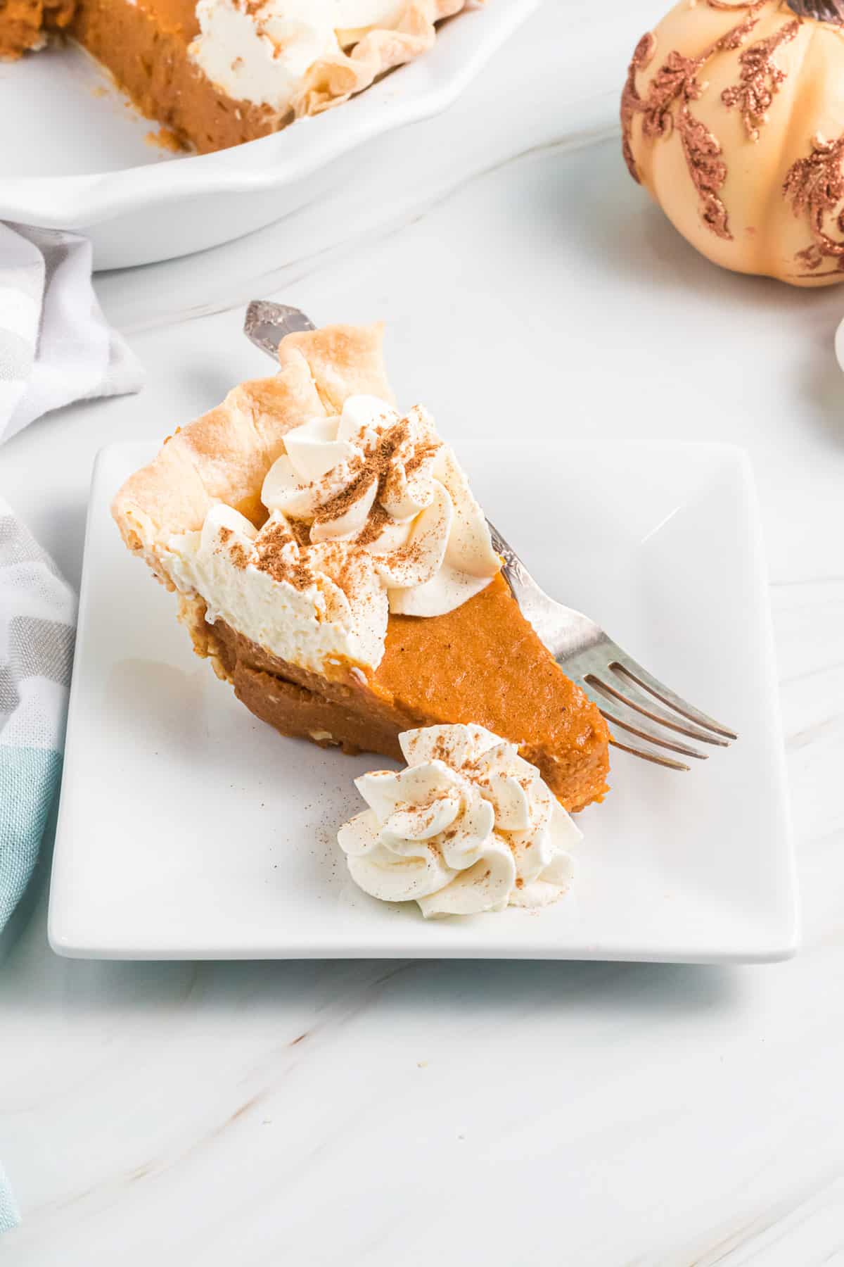 a slice of pumpkin chiffon pie on a white plate with a fork and whipped cream