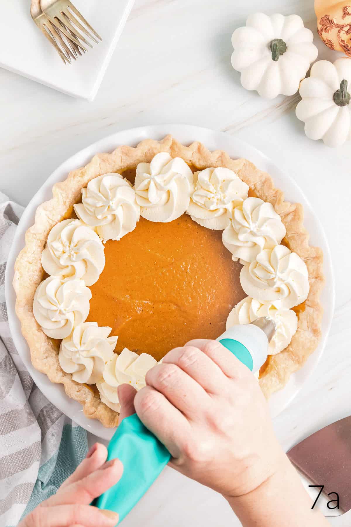 Top view of pumpkin pie being decorated with dollops of whipped cream. 