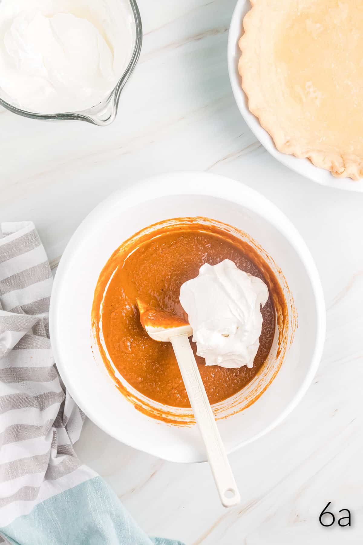 Top view of mixing bowl with pumpkin pie filling it in, with a dollop of meringue in it and a white spatula in the bowl. 