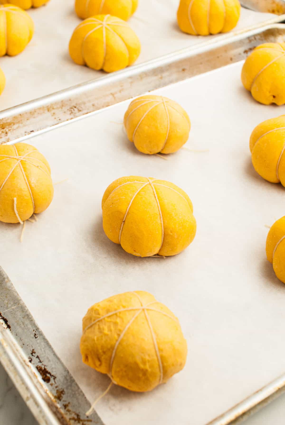 Pumpkin shaped dough balls have risen and have taken on a more pronounced pumpkin shape as they've grown past the twine that gives slight indents into the dough. 