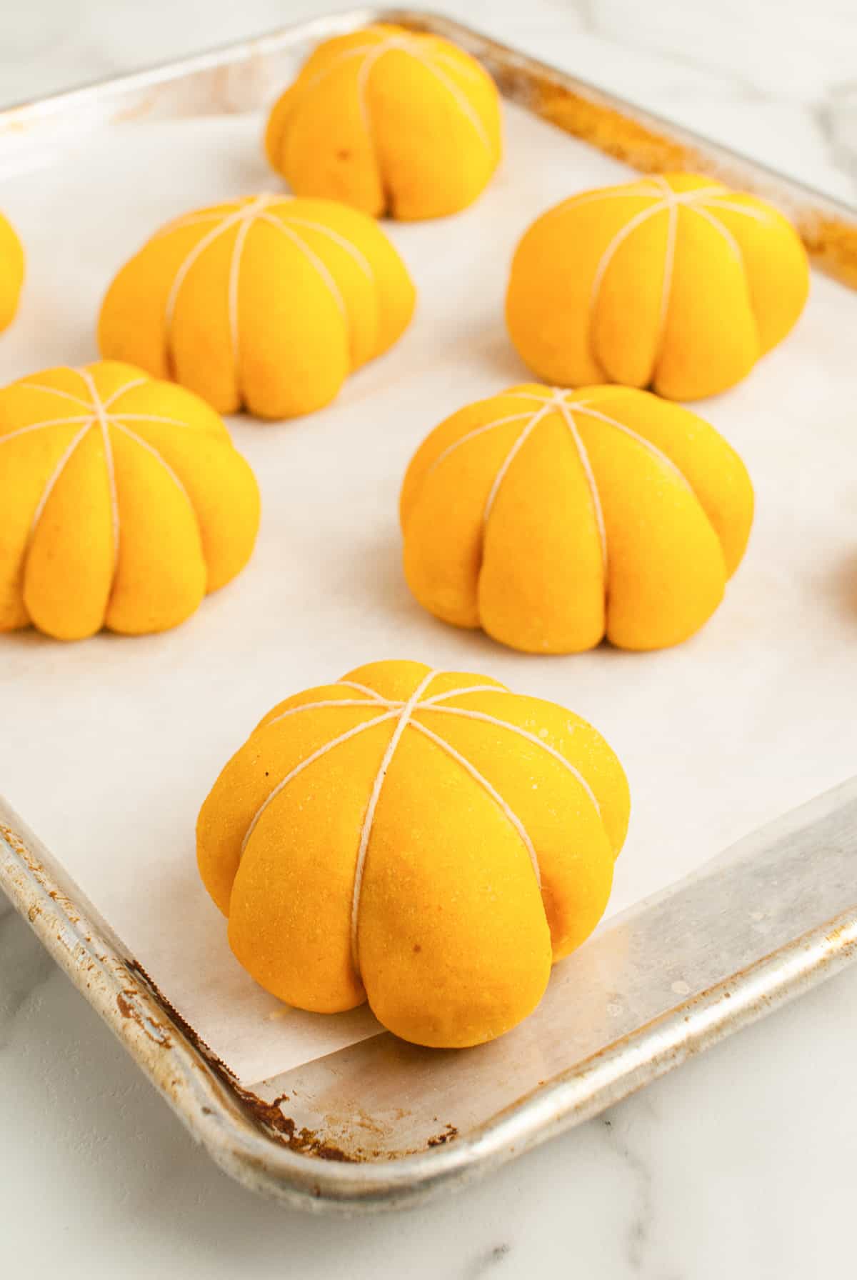 A close up of the pumpkin shaped dough on a baking sheet lined with parchment paper. 