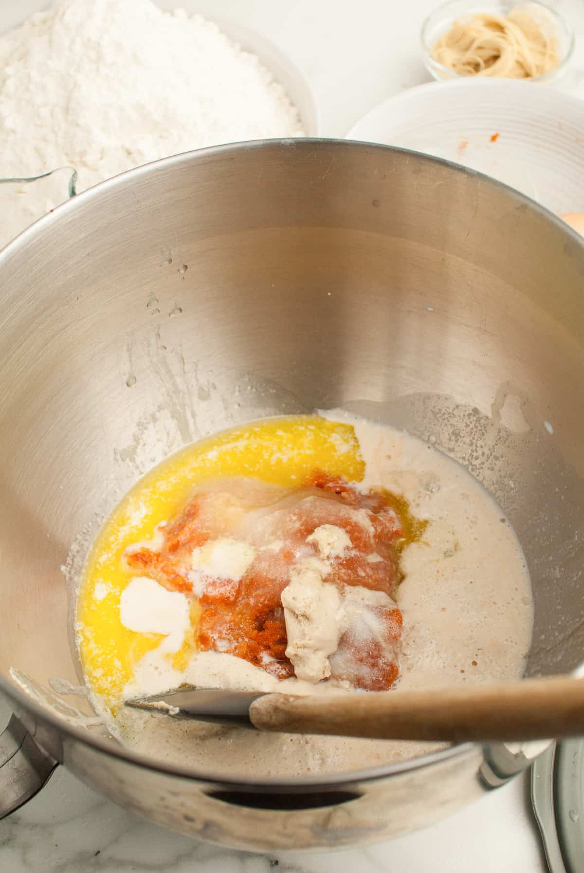 Pumpkin dinner roll ingredients are in the bottom of the bowl of a stand mixer.