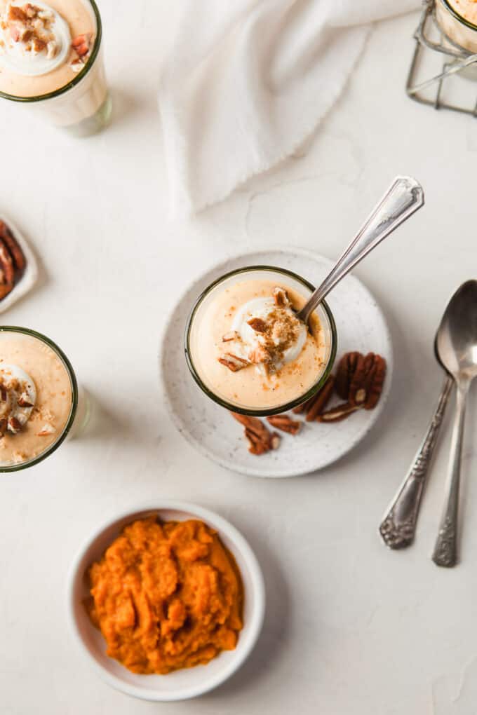 An overhead image of creamy pumpkin mousse in a cup next to a bowl of pumpkin puree.