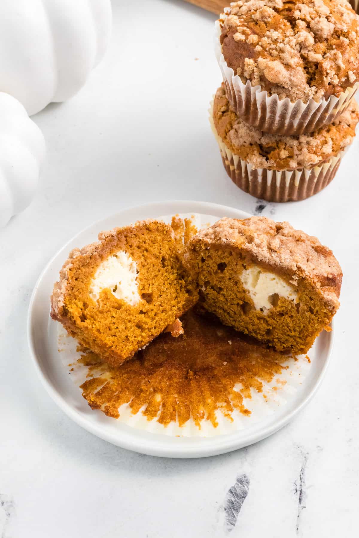 a pumpkin muffin filled with a cream cheese center sliced in half on a plate.