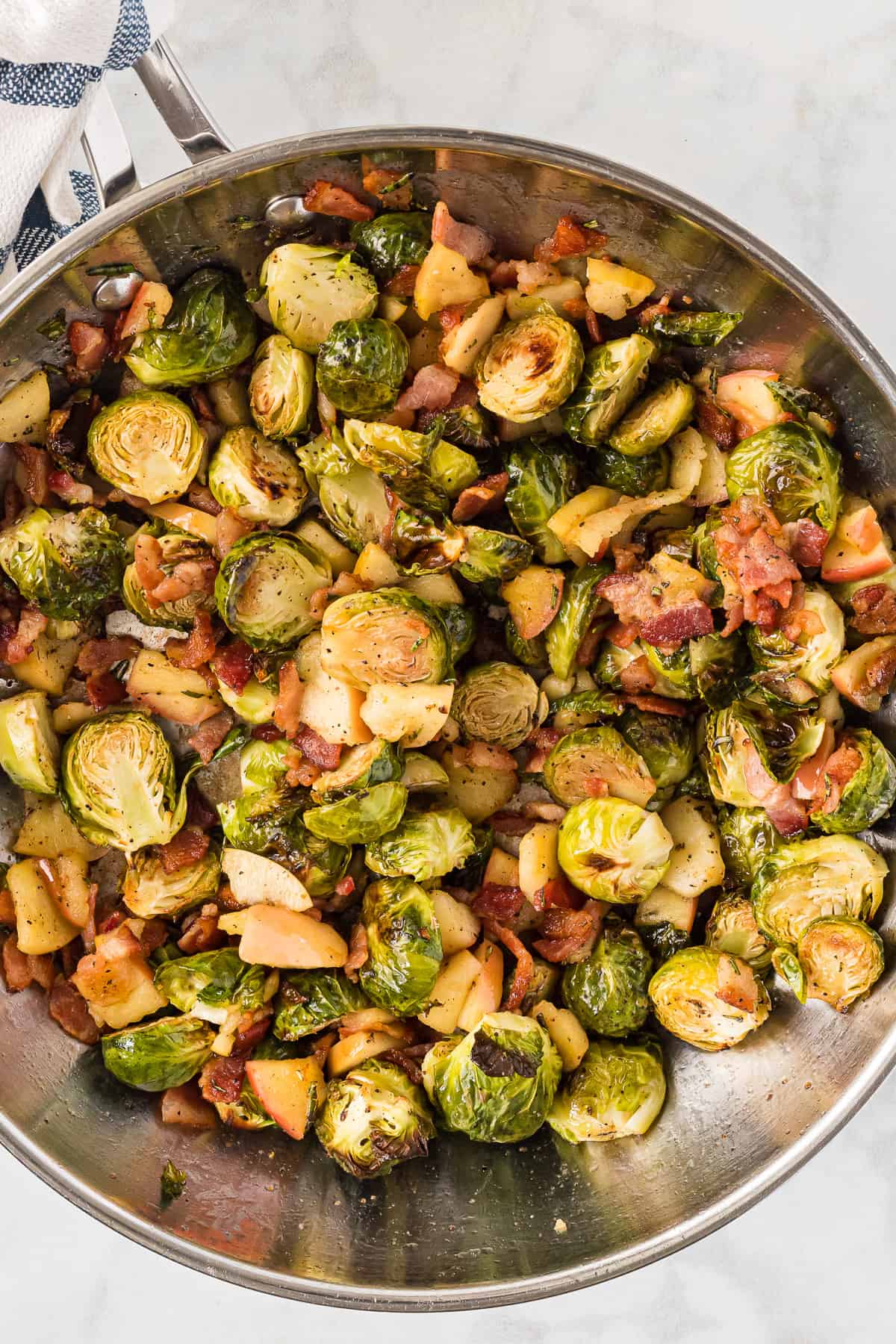 A large metal bowl filled with roasted brussels sprouts being tossed with crispy bacon and sauteed apples.