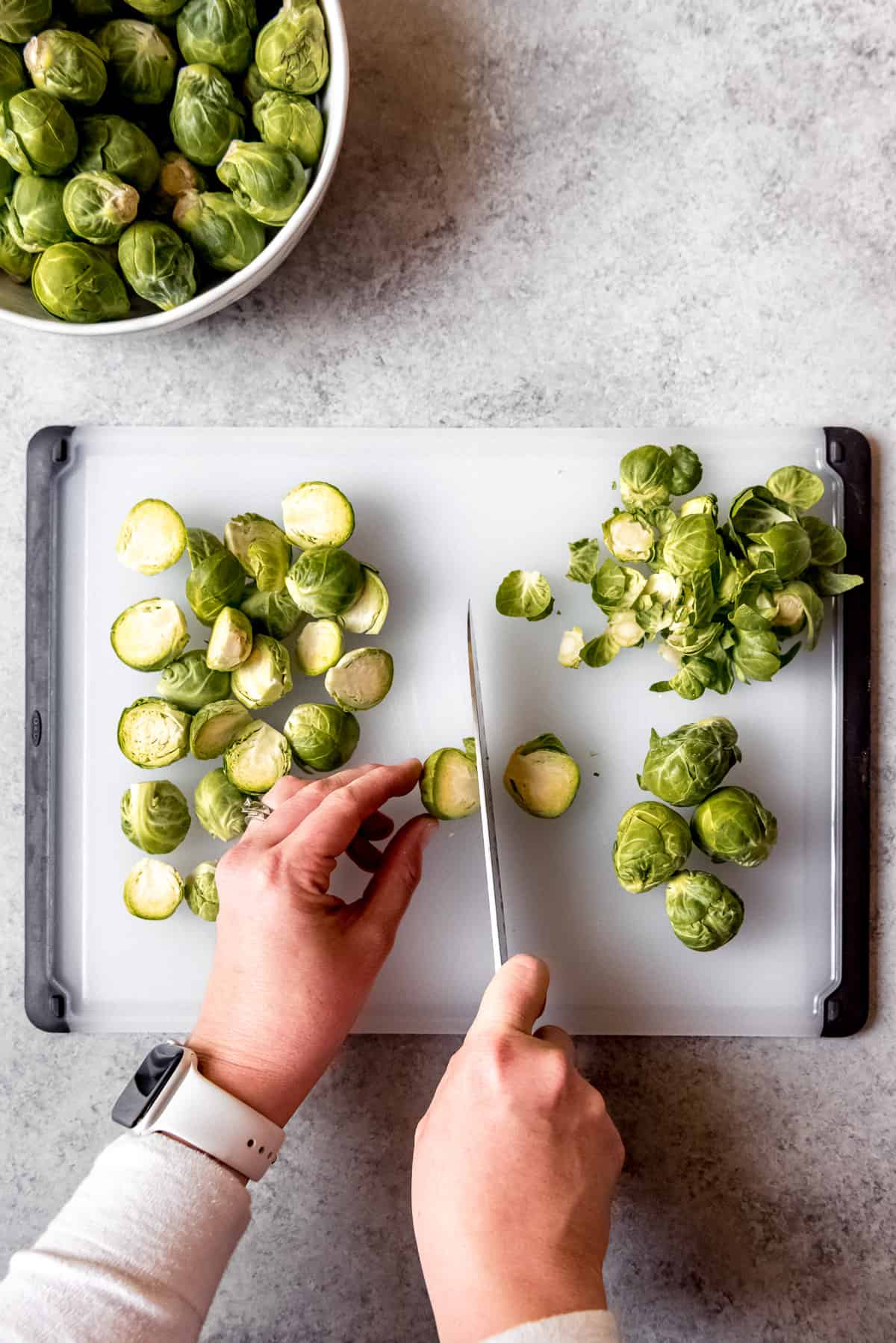 Slicing brussels sprouts in half on a cutting board.