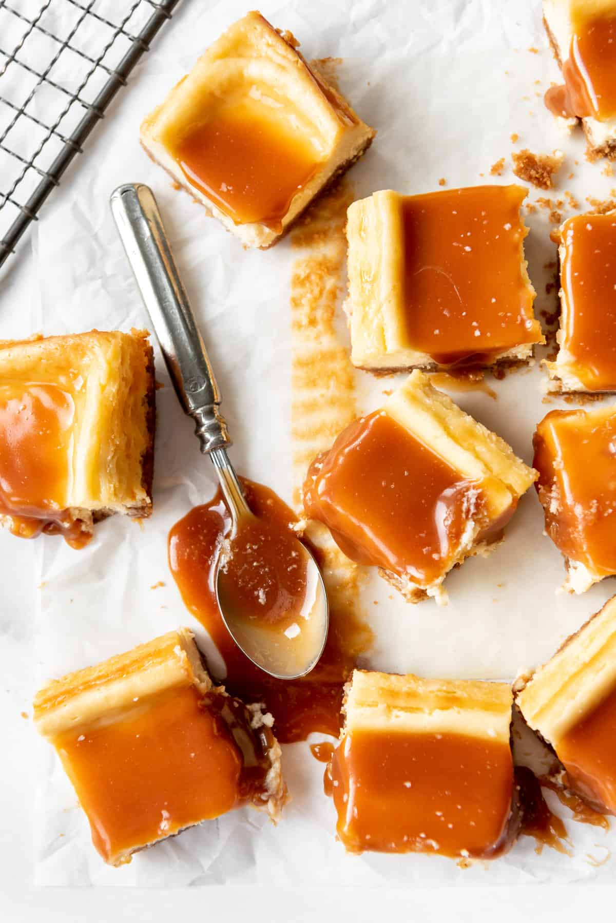 a spoon in a puddle of salted caramel surrounded by salted caramel cheesecake squares.