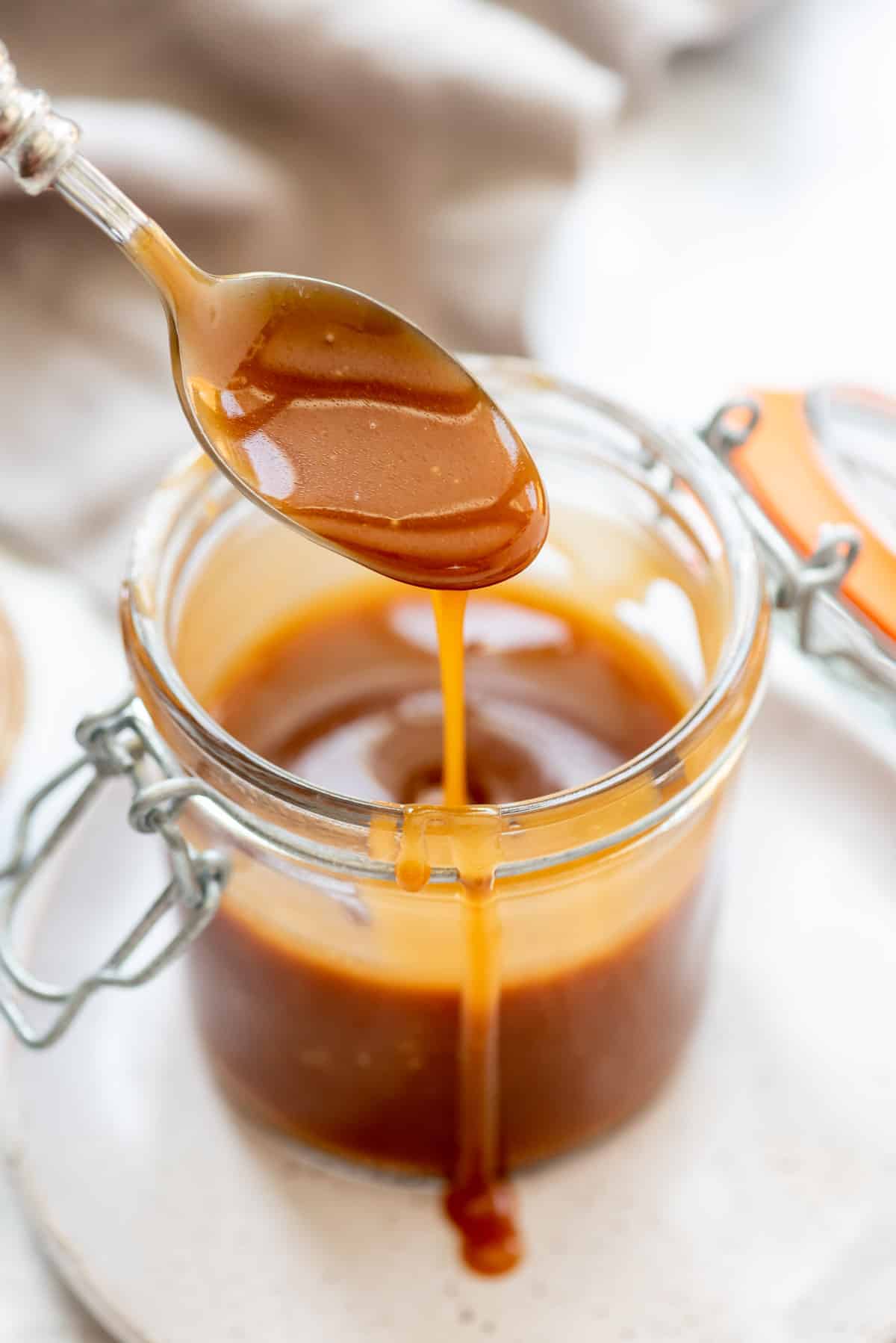 a spoon pouring homemade caramel sauce back into a jar.