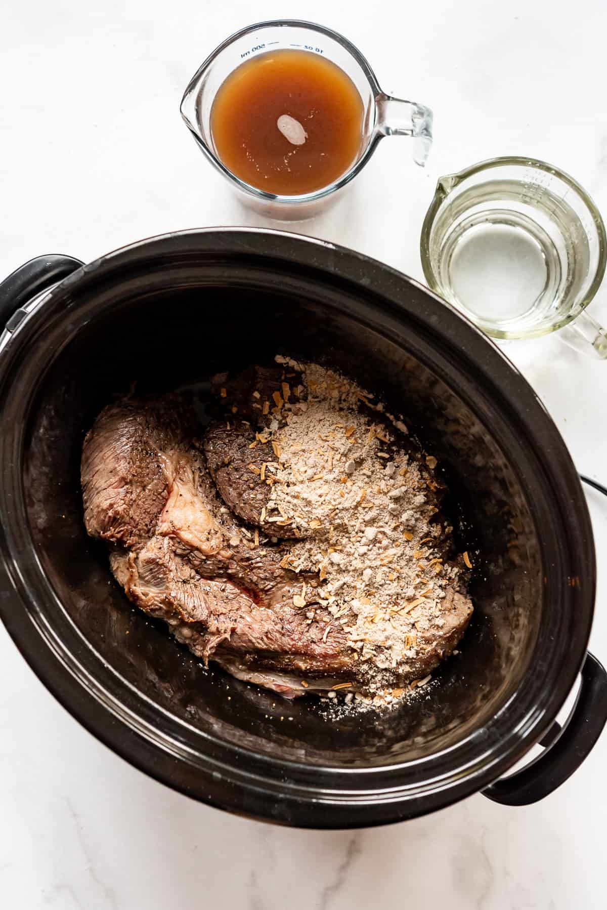 a seared beef chuck roast in a slow cooker with dry onion soup mix sprinkled on top.