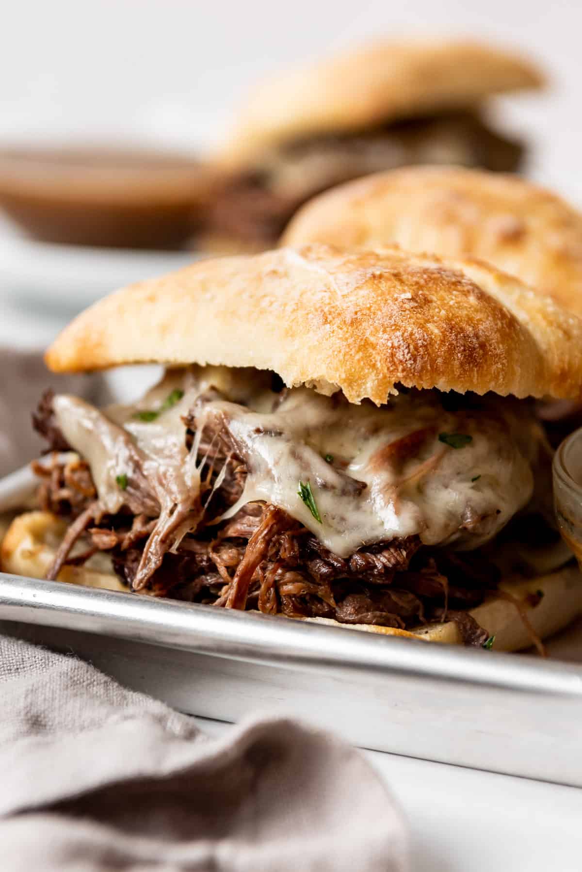 Close up image of the side of a shredded beef sandwich, covered with melted cheese and a ciabatta roll. 