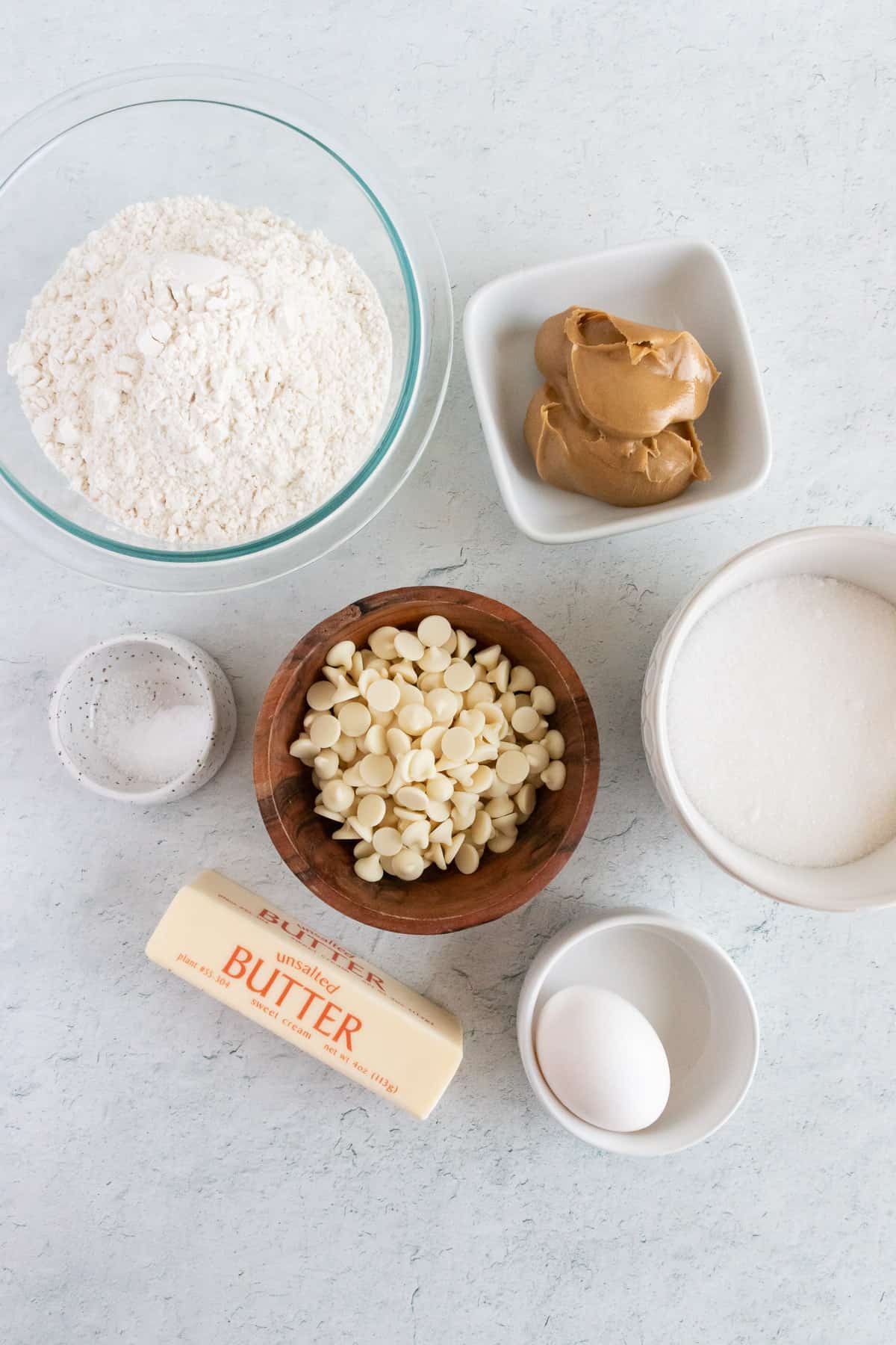 Flour, peanut butter, white chocolate chips, salt, butter, egg, and sugar in individual bowls for making peanut butter white chocolate cookie dough.