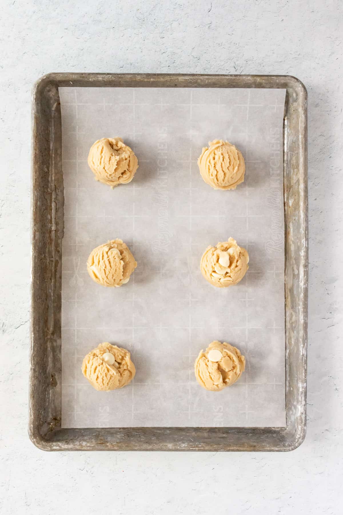 Six balls of dough are evenly spaced on a cookie sheet lined with parchment paper. 