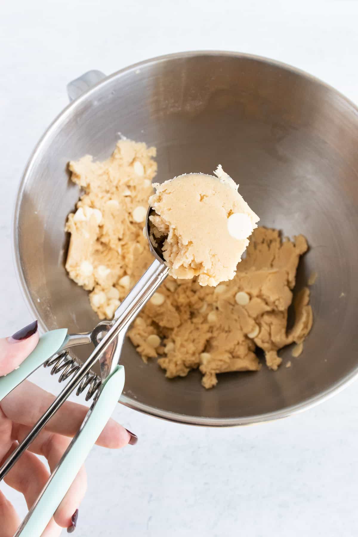 Scooping mixed dough from a metal bowl. 